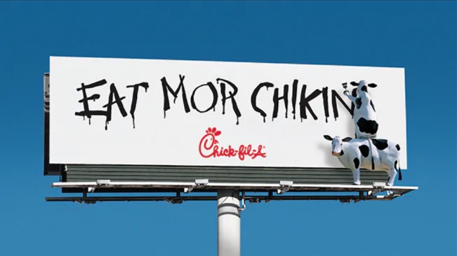 A billboard from Chick-fil-A showing two cows painting a sign that says "Eat more chikin."