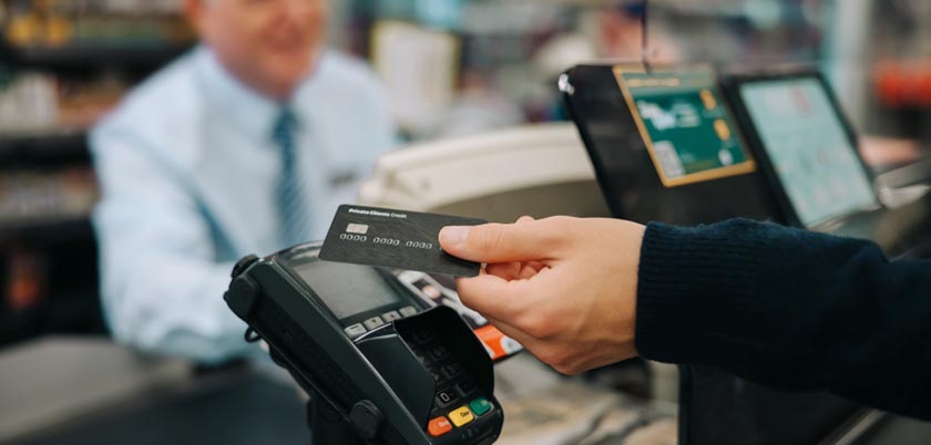 A person's hand holding an NFC-enabled card up to a payment terminal at a cash register.