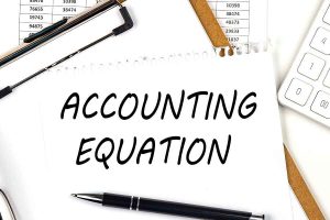 ACCOUNTING EQUATION written on a white paper on top of a clipboard.