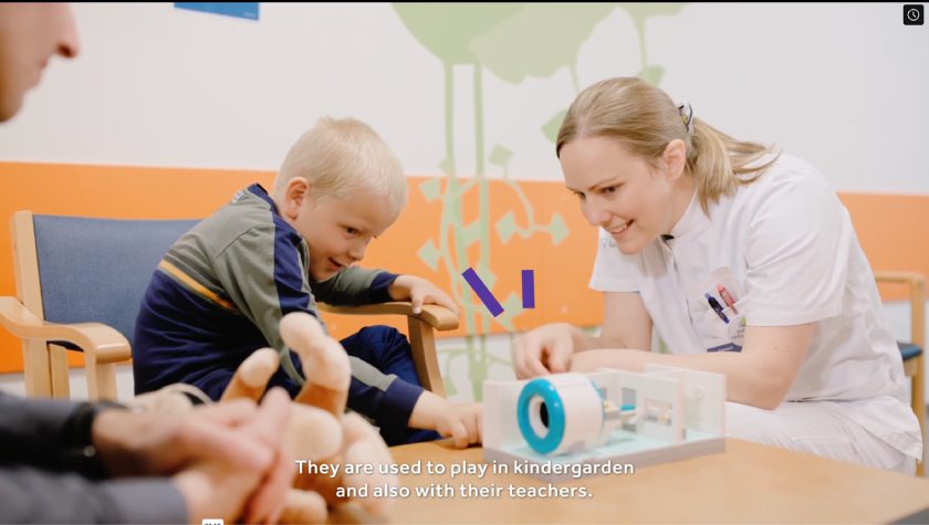 A child and a nurse playing with a LEGO MRI scanner set in a hospital.