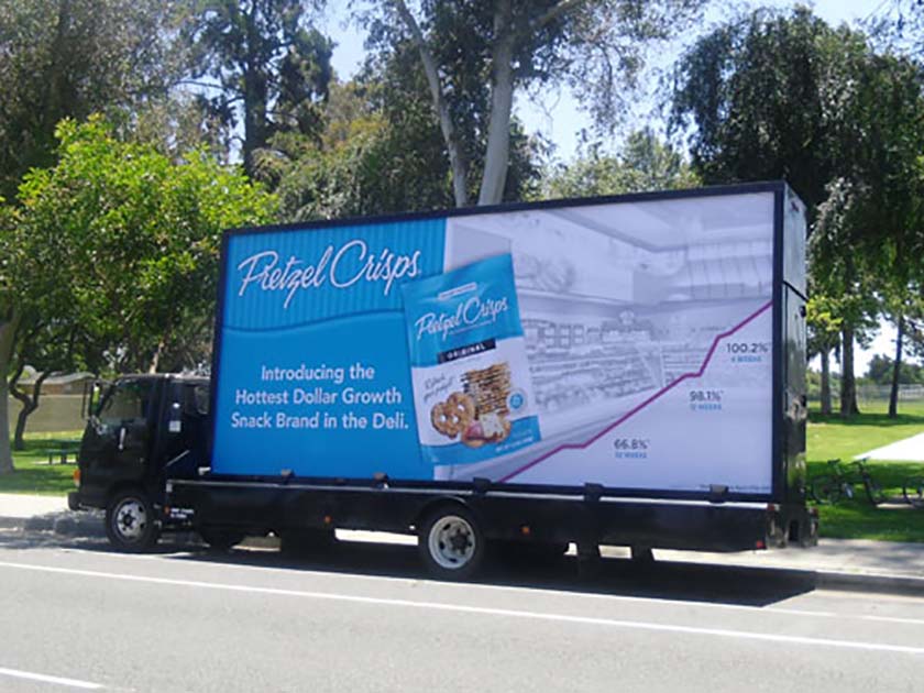 A mobile physical billboard on the side of a truck advertising a pretzel brand.