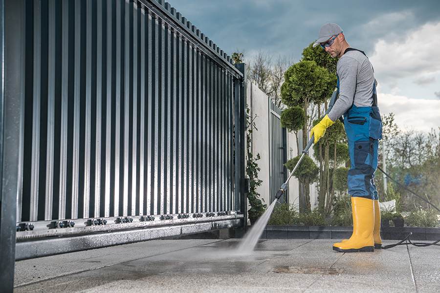 A worker is cleaning the concrete driveway using a pressure washer.