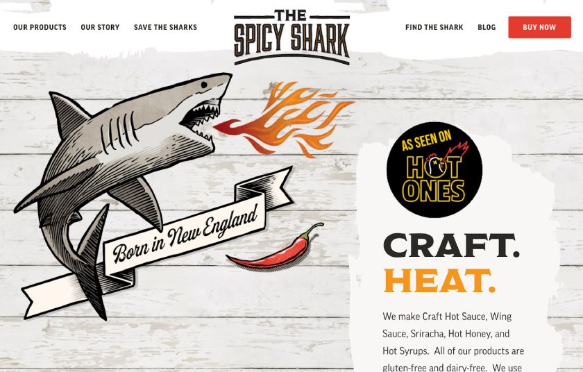 The Spicy Shark home page featuring a shark breathing fire above a banner that says 'Born in New England' on the left, a 'Hot Ones' logo, and a description of its hot sauce on the right.