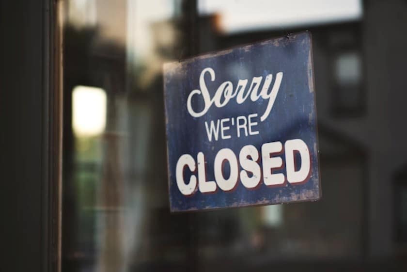 A "Sorry We're Closed" sign hangs in a store window.