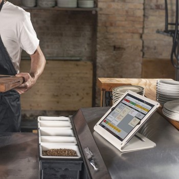 TouchBistro KDS screen tablet sitting on a restaurant kitchen countertop.