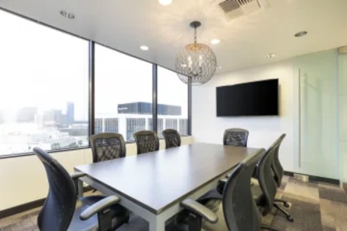 A meeting room with big windows, a television, and a lighting fixture hanging above the table