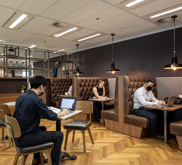 A coworking space with seating booths and three employees on their laptops.