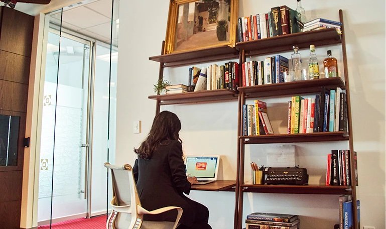 A woman using her laptop at a desk filled with books.