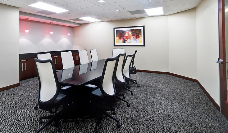 A meeting room with white chairs, a long table, and an art piece hung on one wall.