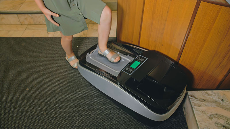 A person using an automatic shoe cover dispenser.