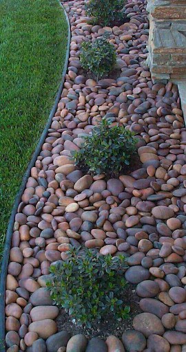 Large multicolored river rocks in a flower bed with edging