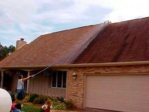 Man pressure washing the roof of a house
