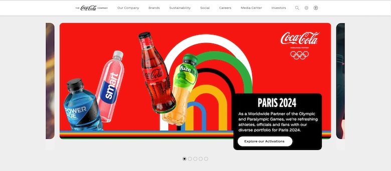 Coca-Cola homepage with deep red hero banner showing four bottles floating in space with arches of Olympic colors in the background with a pop-up for "Paris 2024."