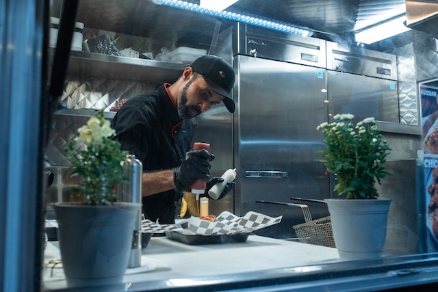 A chef in a food truck topping food with sauce from a squeeze bottle.