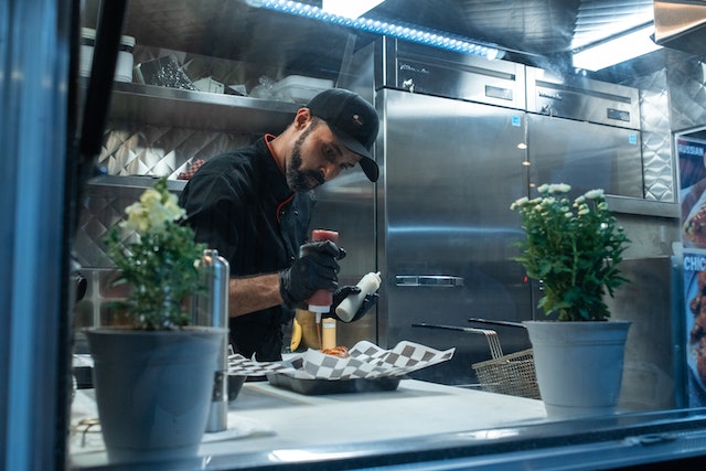 A cook in a food truck squeezing sauce from a squeeze bottle.