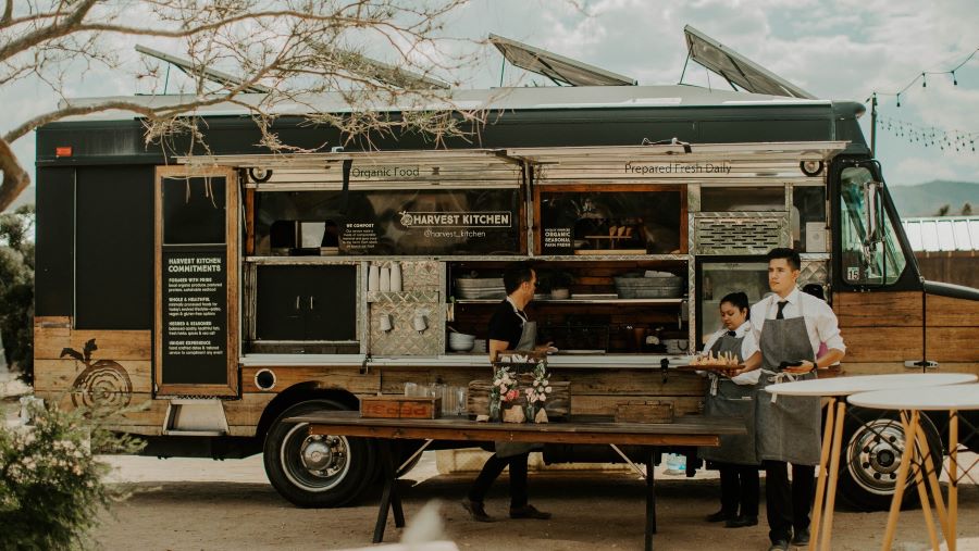 Aproned waiters carrying plates of food outside a food truck.