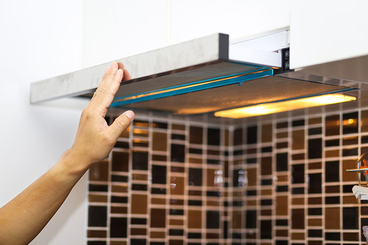A hand touching the surface of a cooking hood in the kitchen.