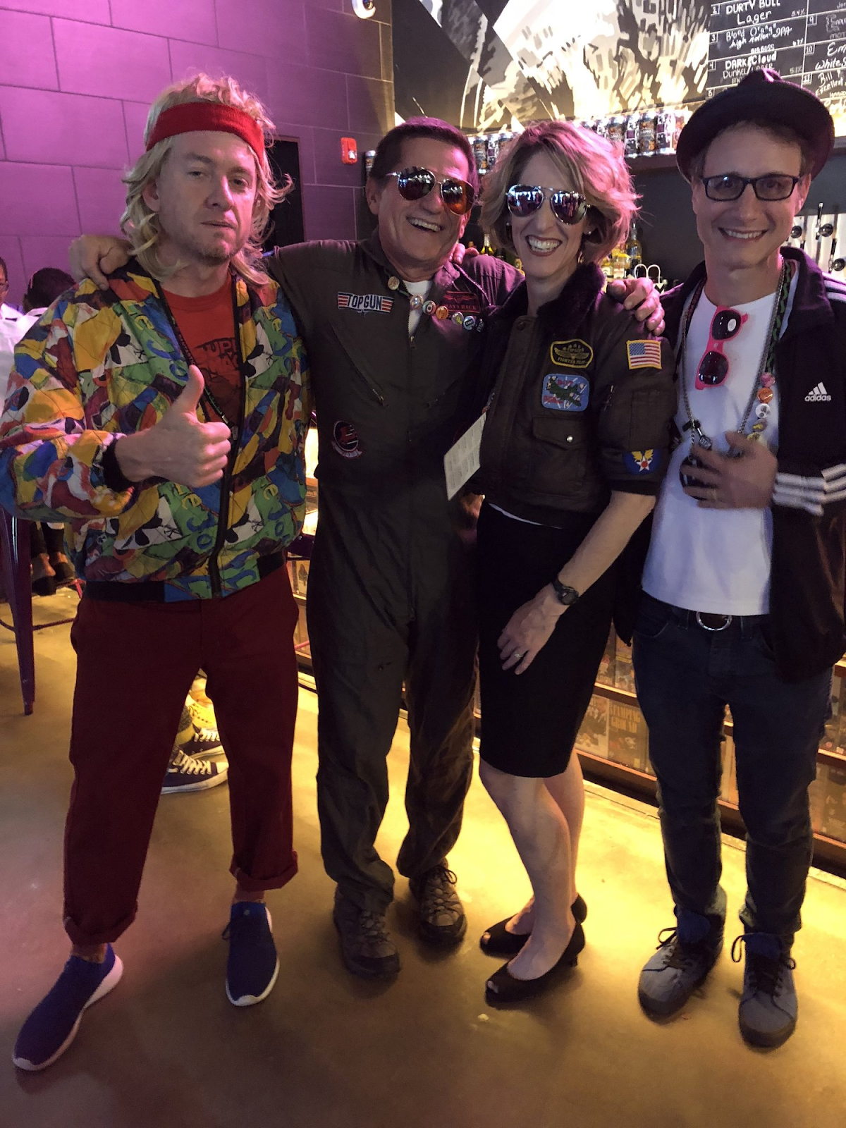 Four people dressed in 1980's costumes at a grand opening party.