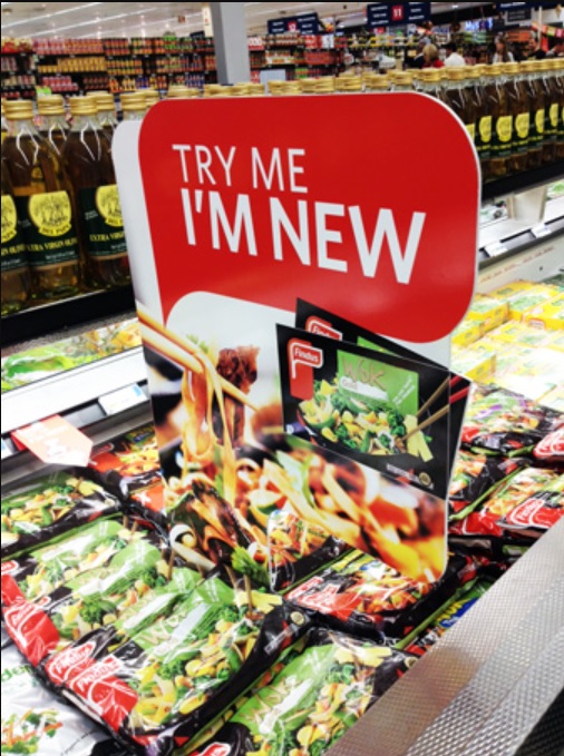 A bright red call to action sign that reads "Try me I'm new" positioned above a display of food items.