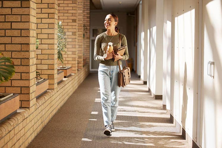 Image of a woman walking while holding study materials