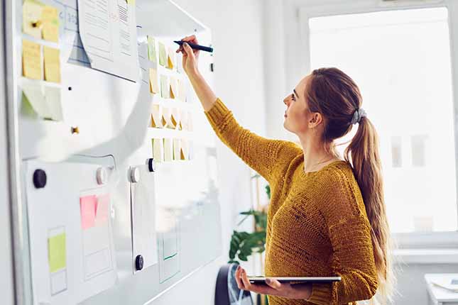 A woman writing on a whiteboard that is filled with post-its