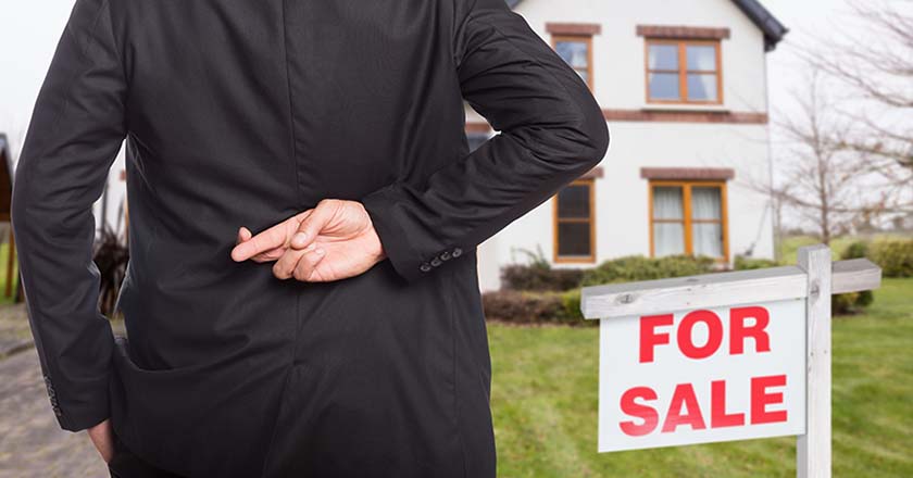 Person crossing fingers behind back in front of a house for sale 