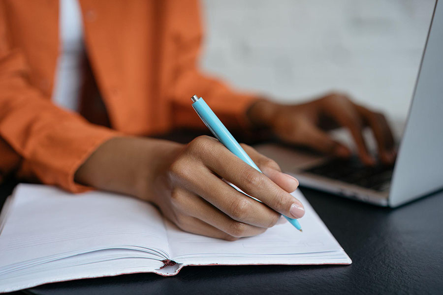 Image of person taking notes on pen and paper plus computer