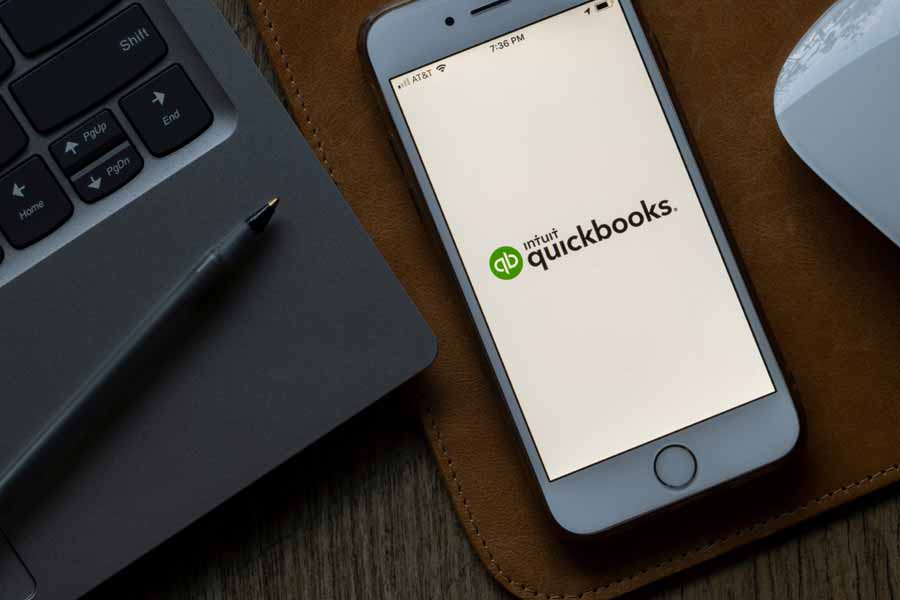 Quickbooks Online logo seen on a mobile phone screen beside a laptop.