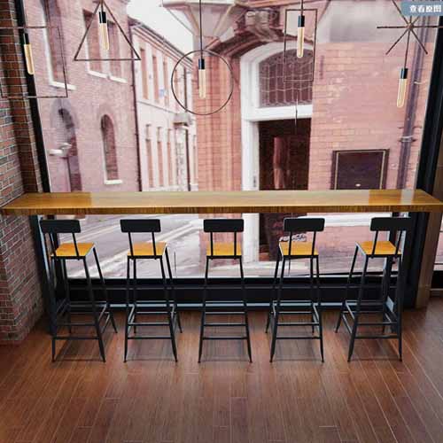 Wooden counter with five barstools against a window.