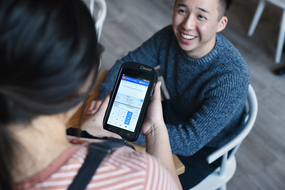 A server rings in a sale tableside on a Toast Go 2 handheld POS device