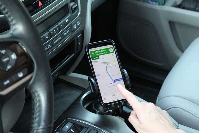 Phone holder in cup holder with phone that is mapping person and person is about to touch screen.