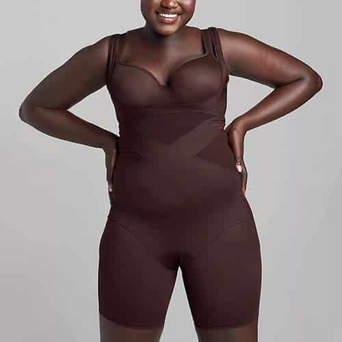 Woman wearing brown shapewear bodysuit with shorts on gray background