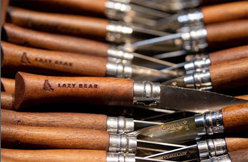 Line of steak knives embossed with Lazy Bear restaurant logo.