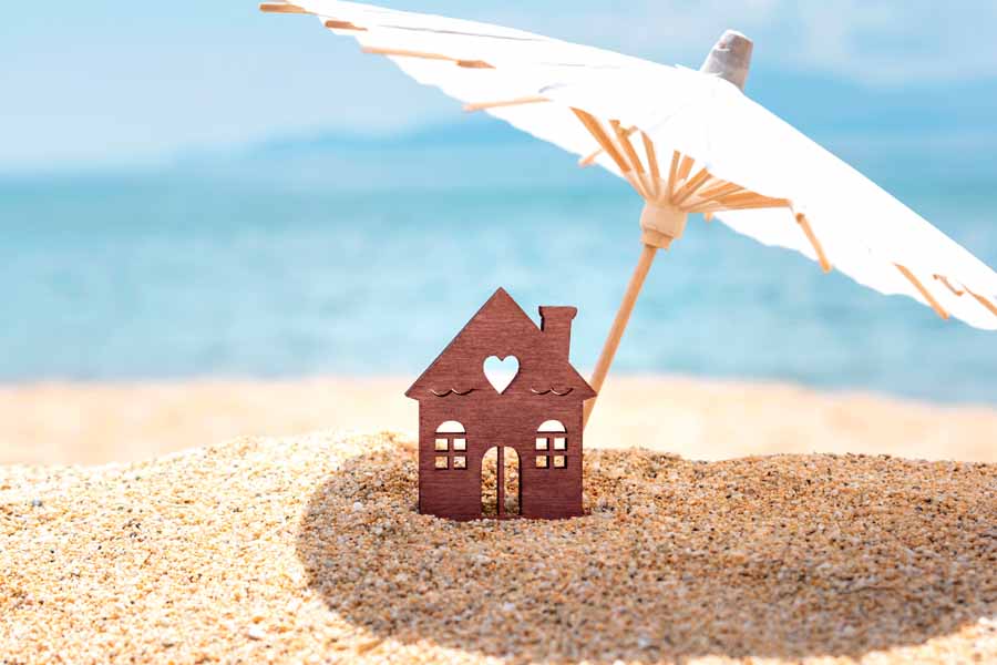 Miniature house and umbrella on beach.