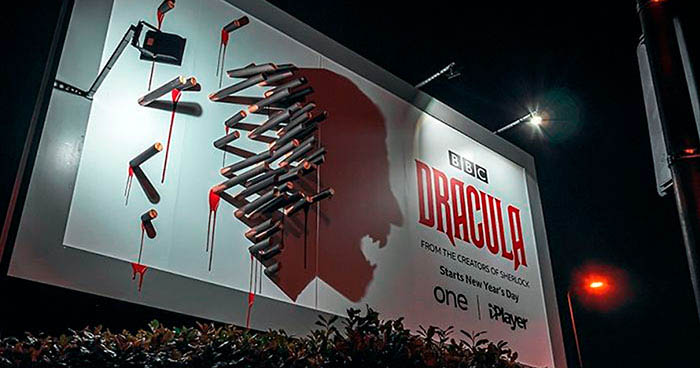 BBC's billboard for its TV show "Dracula" at nighttime, showing a collection of bloody stakes collectively depicting a shadow of a vampire.