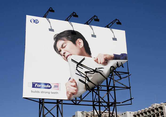 Formula toothpaste billboard with person biting off the billboard for slogan "builds strong teeth"