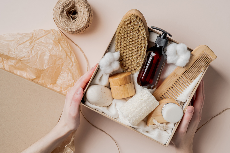 Person holding a cardboard box with soaps, brushes, and other bathroom supplies. 