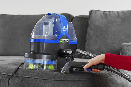 Blue and black upholstery cleaner being used on dark grey couch.