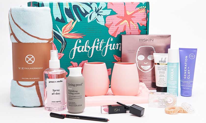 FabFitFun Box with content in front of box, including face mask, blanket, and other beauty supplies. 