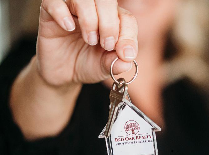 Hand holding a key with Red Oak Realty logo.