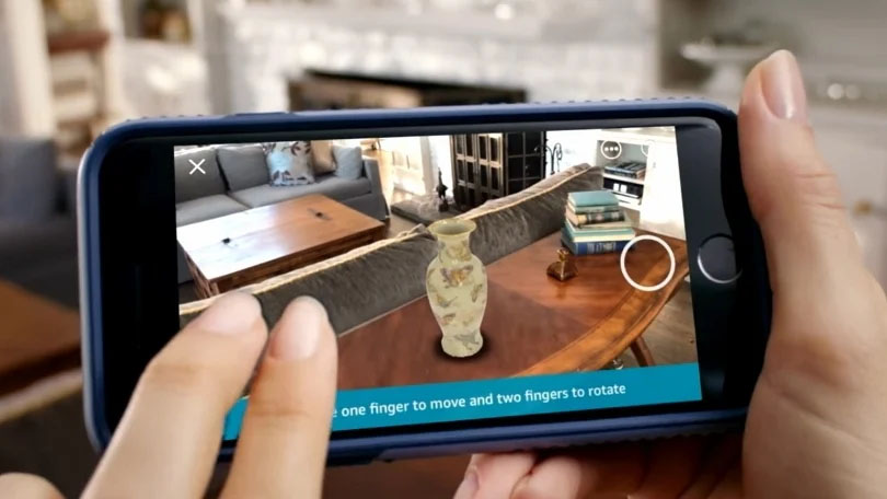 A person's hands holding a smartphone displaying an augmented reality view of their room, with a virtual pot placed on a table.
