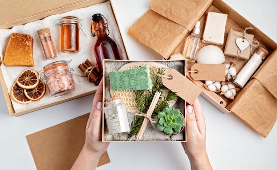 Person holding plant-themed box over two other boxes filled with bottles of soaps and other bathroom trinkets.