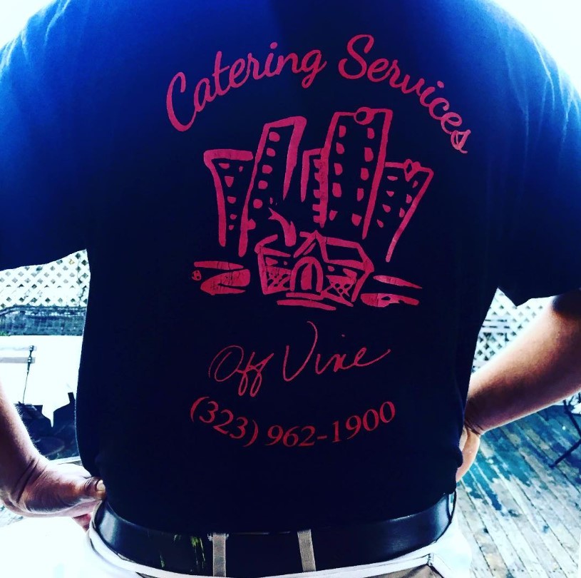 Server wearing a black t-shirt with a red catering logo and phone number on the back.