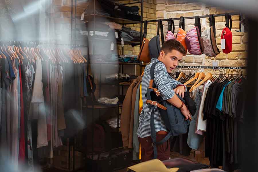 Boy in blue checked shirt in a store putting a product into his backpack sneakily.