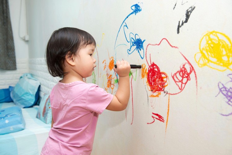 Young child drawing on the walls with crayons.