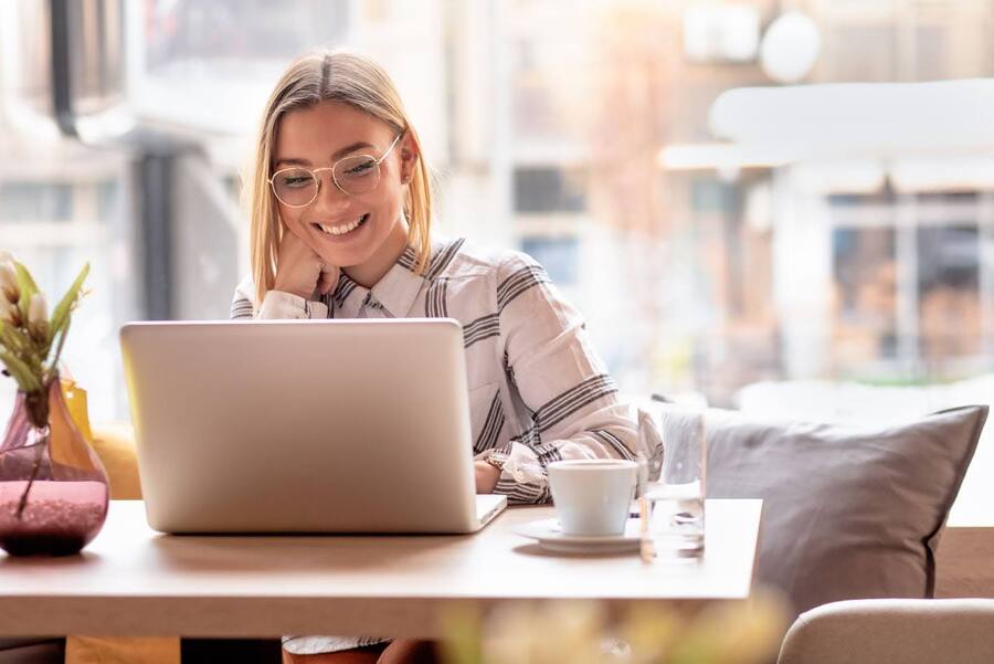 Woman smiling into computer while drinking coffee.