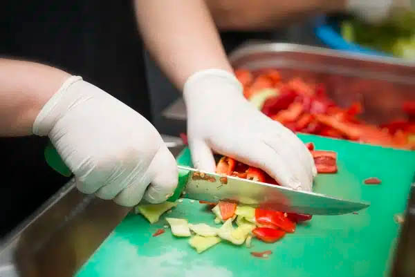 Chopping vegetables with gloved hands.