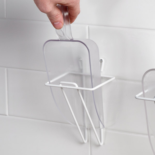 Putting clear plastic scoop into a white wire wall-hung hanger.