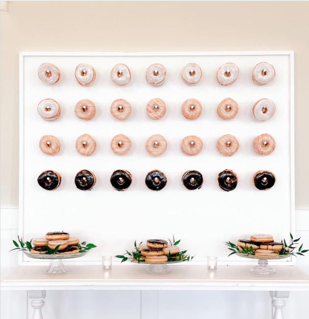 Donuts hung on a peg board as a food wall with plates of donuts arranged below.