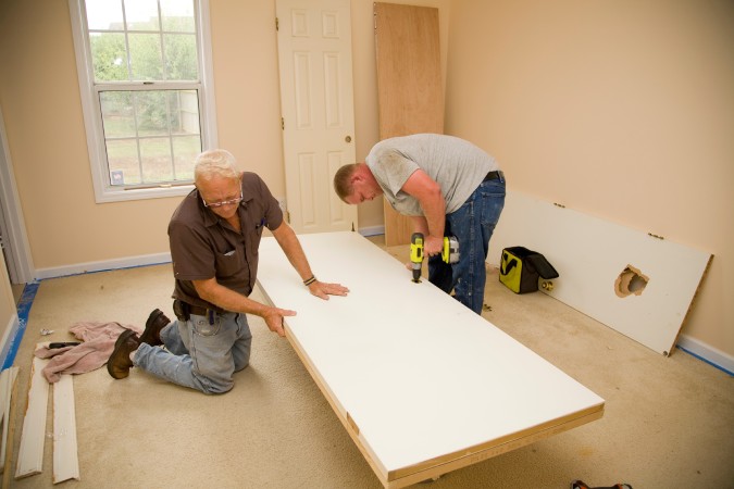 Two property owners fixing a door on their property.